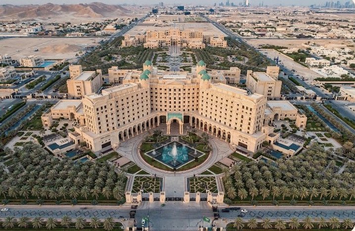 Aerial view of a palace complex with central fountain and palm gardens